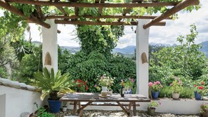A wooden pergola with a table set for dining, surrounded by potted plants and flowers.