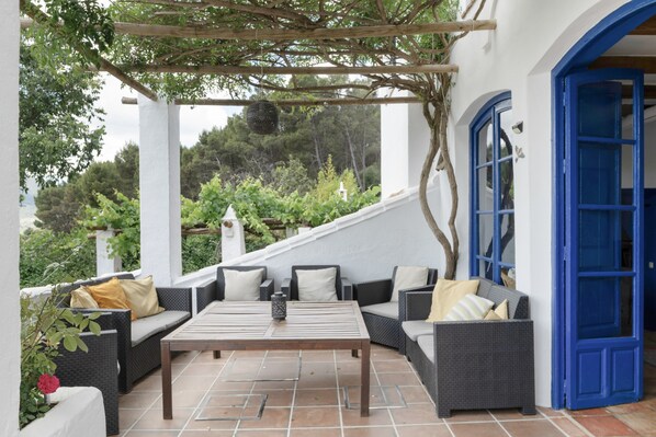 An outdoor patio with wicker furniture, a wooden table, and a blue door.