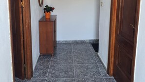 A hallway with a tiled floor, a wooden cabinet with a plant, and a framed picture on the wall.