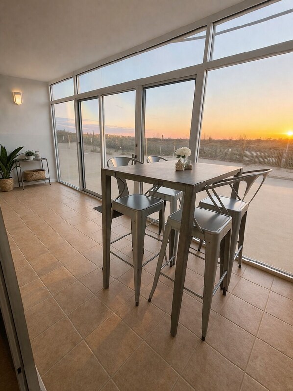 A dining area with a table and chairs, large windows, and a view of the sunset. - Walk-Out to Sand - Oceanfront Condo (Ocean City)