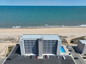 A multi-story hotel with a parking lot and a pool. - Walk-Out to Sand - Oceanfront Condo (Ocean City)
