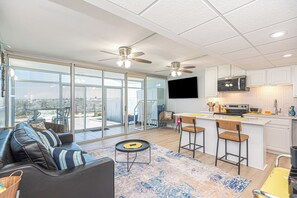 A modern kitchen with a flat-screen TV, a microwave, and a bar area with stools. - Walk-Out to Sand - Oceanfront Condo (Ocean City)
