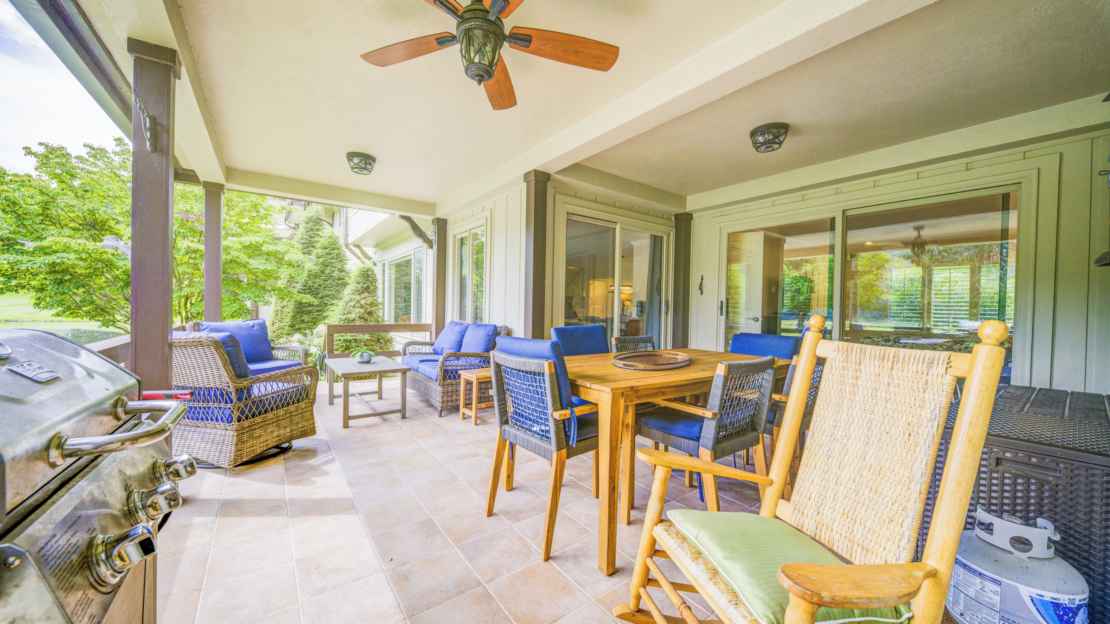 A covered patio area with outdoor furniture, a grill, and a ceiling fan.