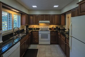 A kitchen with dark wooden cabinets, a white stove, and a refrigerator. - Lakeside Living - Stunning lakeside condo in Hound Ears community. (Boone)