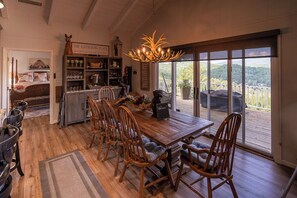 A dining area with a wooden table and chairs, a chandelier, and a view through large windows. - Breathtaking Grandfather View has a truly Breathtaking view of Grandfather Mount (Boone)