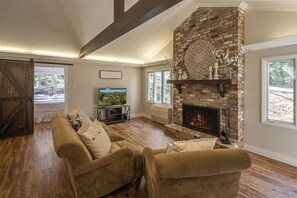 A living room with a fireplace, wooden floors, a sofa, and a television. - Serenity on Dogwood is nestled within a wooded section of Hound Ears community. (Boone)