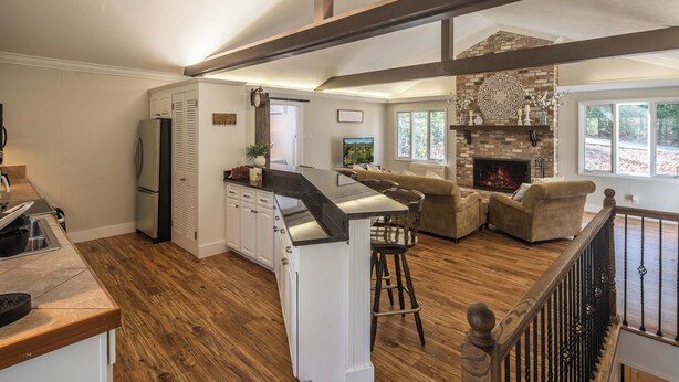 A spacious kitchen with a central island, a dining area with a fireplace, and a living room with a large window. - Serenity on Dogwood is nestled within a wooded section of Hound Ears community. (Boone)