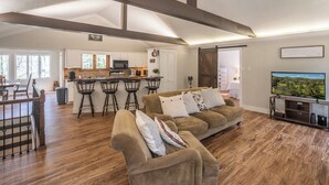 A spacious living area with a sofa, a TV, and a kitchen in the background. - Serenity on Dogwood is nestled within a wooded section of Hound Ears community. (Boone)