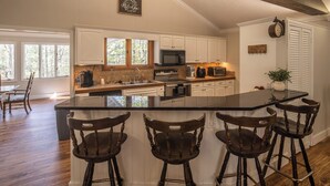 A kitchen with a large island, wooden chairs, and white cabinetry. - Serenity on Dogwood is nestled within a wooded section of Hound Ears community. (Boone)