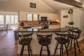 A kitchen with a large island, wooden chairs, and white cabinetry. - Serenity on Dogwood is nestled within a wooded section of Hound Ears community. (Boone)