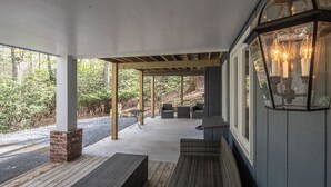 A covered porch with wicker furniture, a brick column, and a lantern. - Serenity on Dogwood is nestled within a wooded section of Hound Ears community. (Boone)