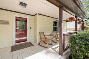 Eine Veranda mit Holzschaukelstühlen, einer Tür mit Fensterfüllung und hängenden Blumenkörben.