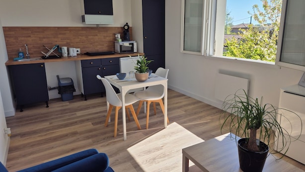A modern kitchen with a microwave, toaster, and sink. There is a dining area with a table and chairs. A large window provides a view of greenery outside.