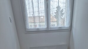 A corner room with a white cushioned bench, a window with sheer curtains, and a wooden floor.