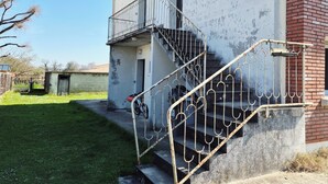 A building with a metal staircase leading to a balcony, a small shed, and a grassy area.