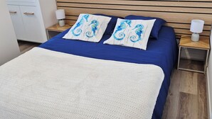 A bedroom with a bed, two nightstands, a wooden headboard, a white wall, and a door.