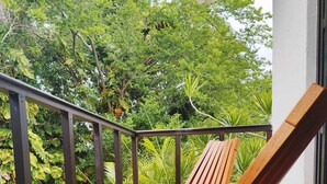 A wooden lounge chair on a tiled patio with a metal railing, surrounded by lush greenery. - Villa in Playacar with a view of the golf course—5-minute walk to the beach and 5th Avenue (Playa del Carmen)
