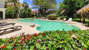 A pool area with lounge chairs, palm trees, and a building with a red roof. - Villa in Playacar with a view of the golf course—5-minute walk to the beach and 5th Avenue (Playa del Carmen)