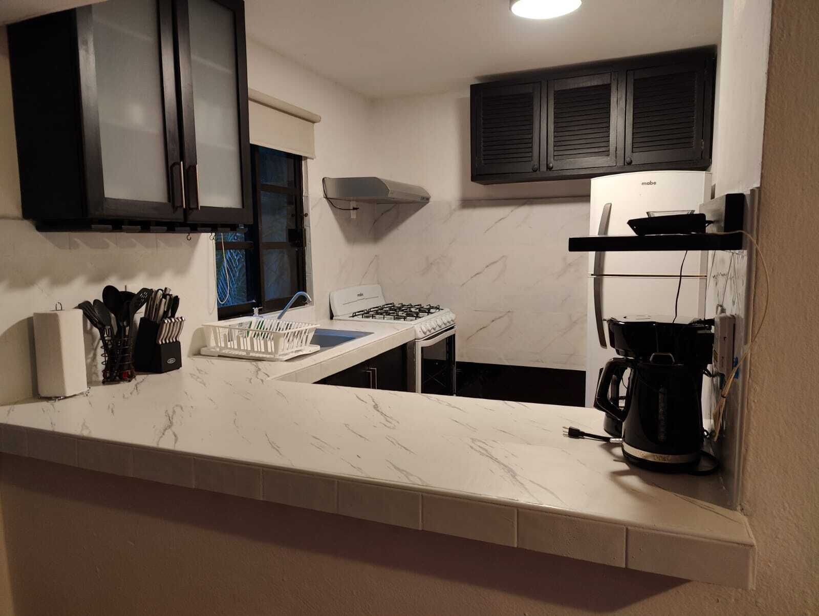 A kitchen with a white countertop, black cabinets, a stove, and a coffee maker.