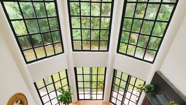 A high-ceiling room with large windows, a brown leather sofa, a wooden coffee table, and a fireplace. - Villa in Playacar with a view of the golf course—5-minute walk to the beach and 5th Avenue (Playa del Carmen)