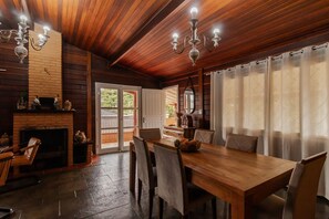 A wooden interior with a fireplace, dining table, chairs, and a chandelier. - Casa Grande c Lareira e Churrasqueira - Cascatinha (Campos do Jordão)