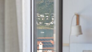 A view through a window of a building with solar panels on the roof, a boat on the water, and a mountainous landscape in the distance.