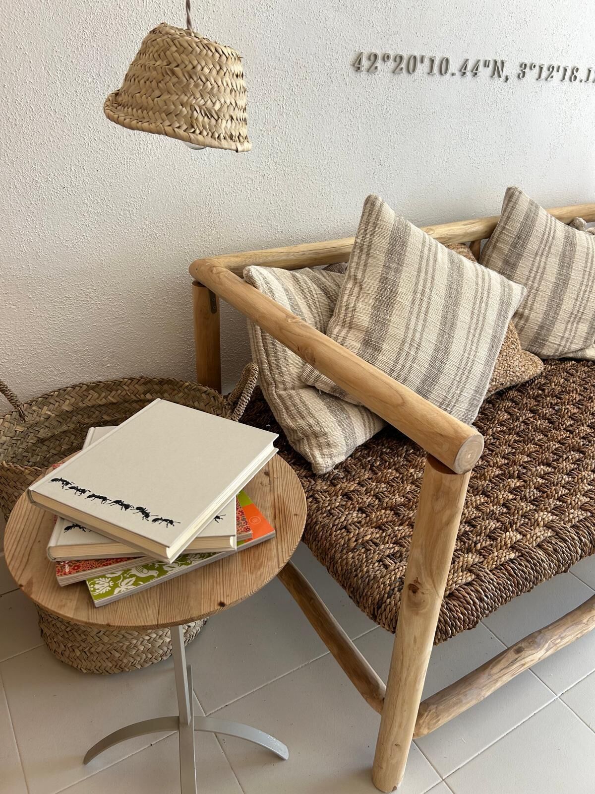 Un rincón acogedor con un sillón tejido, una mesita redonda con libros e iluminación colgante.