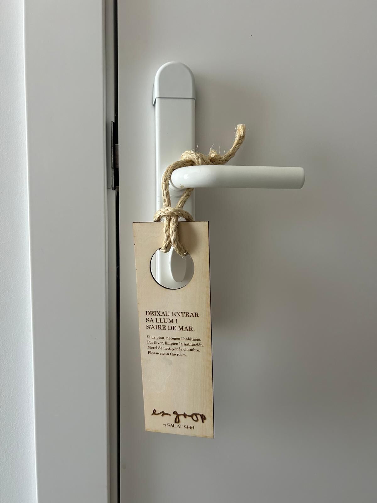 A door with a white handle and a tag attached to it. The tag has text in multiple languages requesting room cleaning.