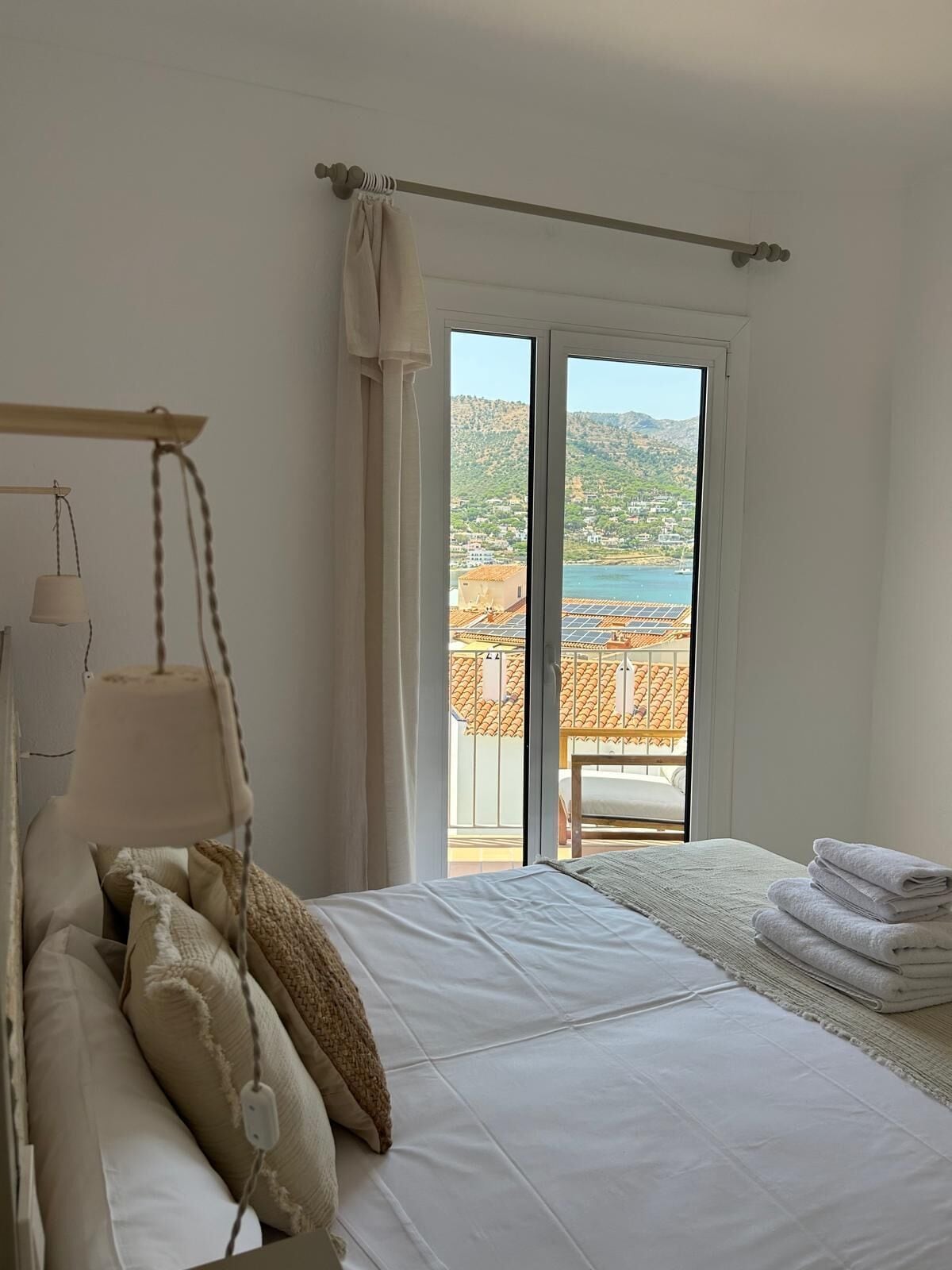 Un dormitorio con cama, una lámpara colgante, vistas a un balcón con paneles solares y una ventana con cortinas.