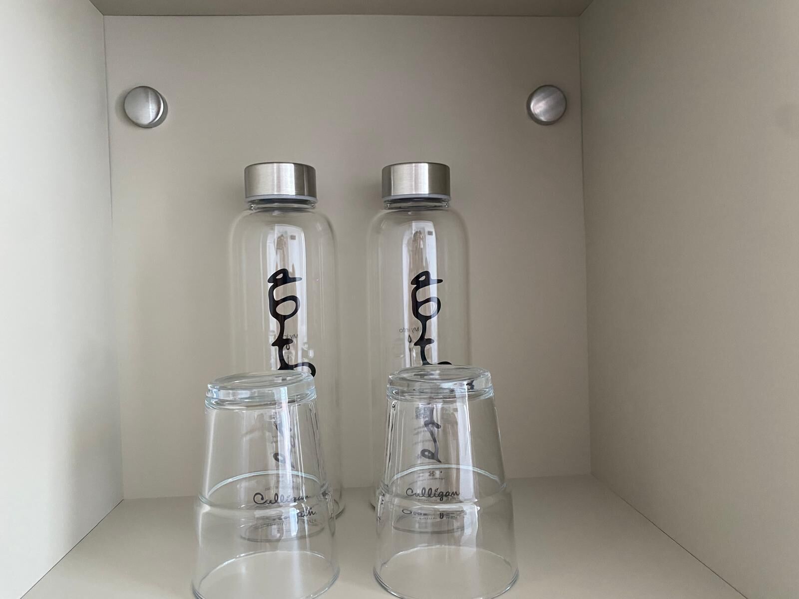 Deux bocaux en verre avec des couvercles en métal et du texte noir, posés sur une étagère blanche.