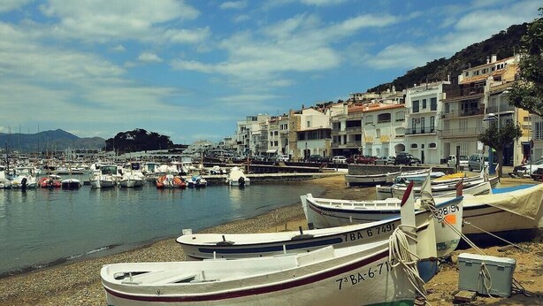 A marina with boats docked, a beach, and buildings along the shore.