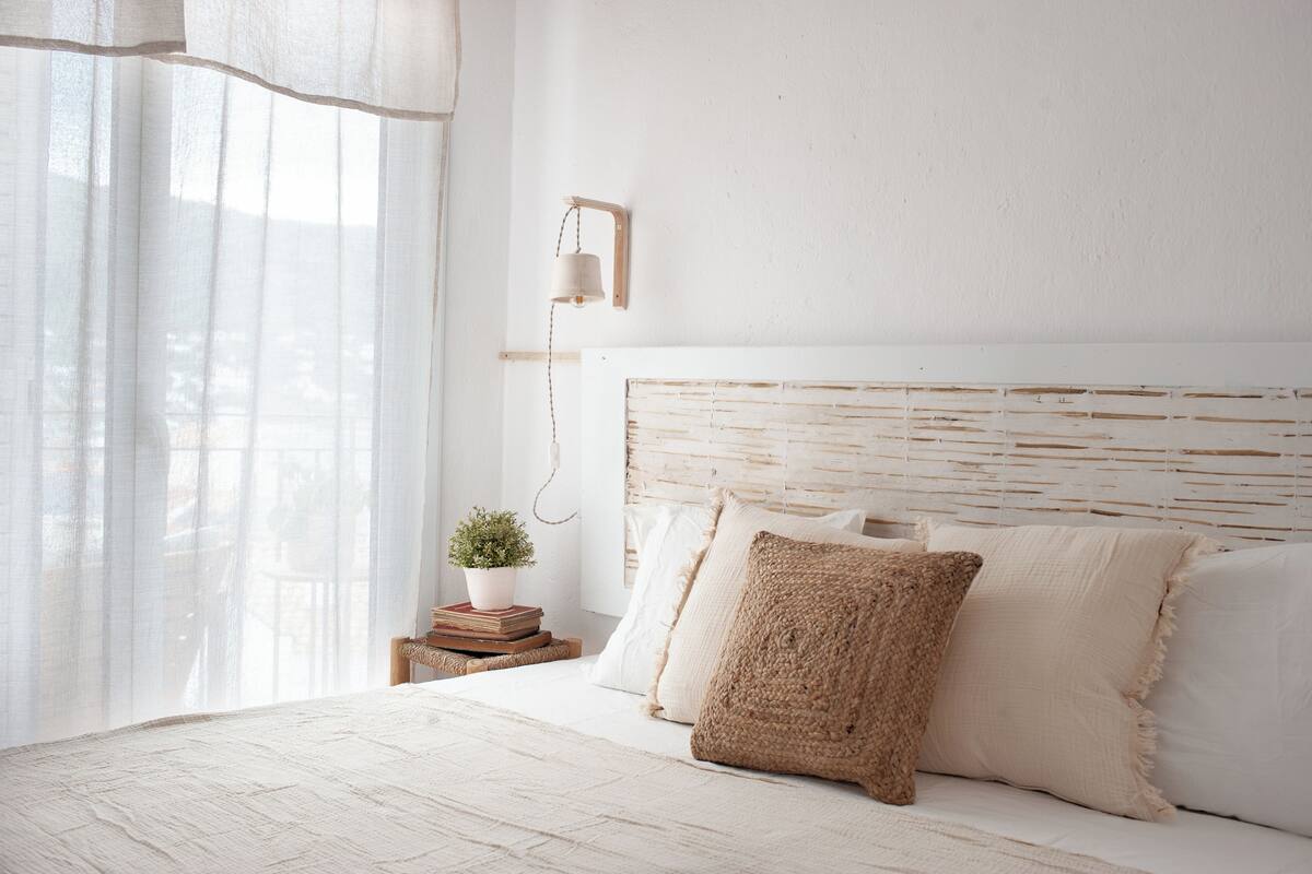A bedroom with a bed, a bedside table with a plant, and a wall-mounted lamp.