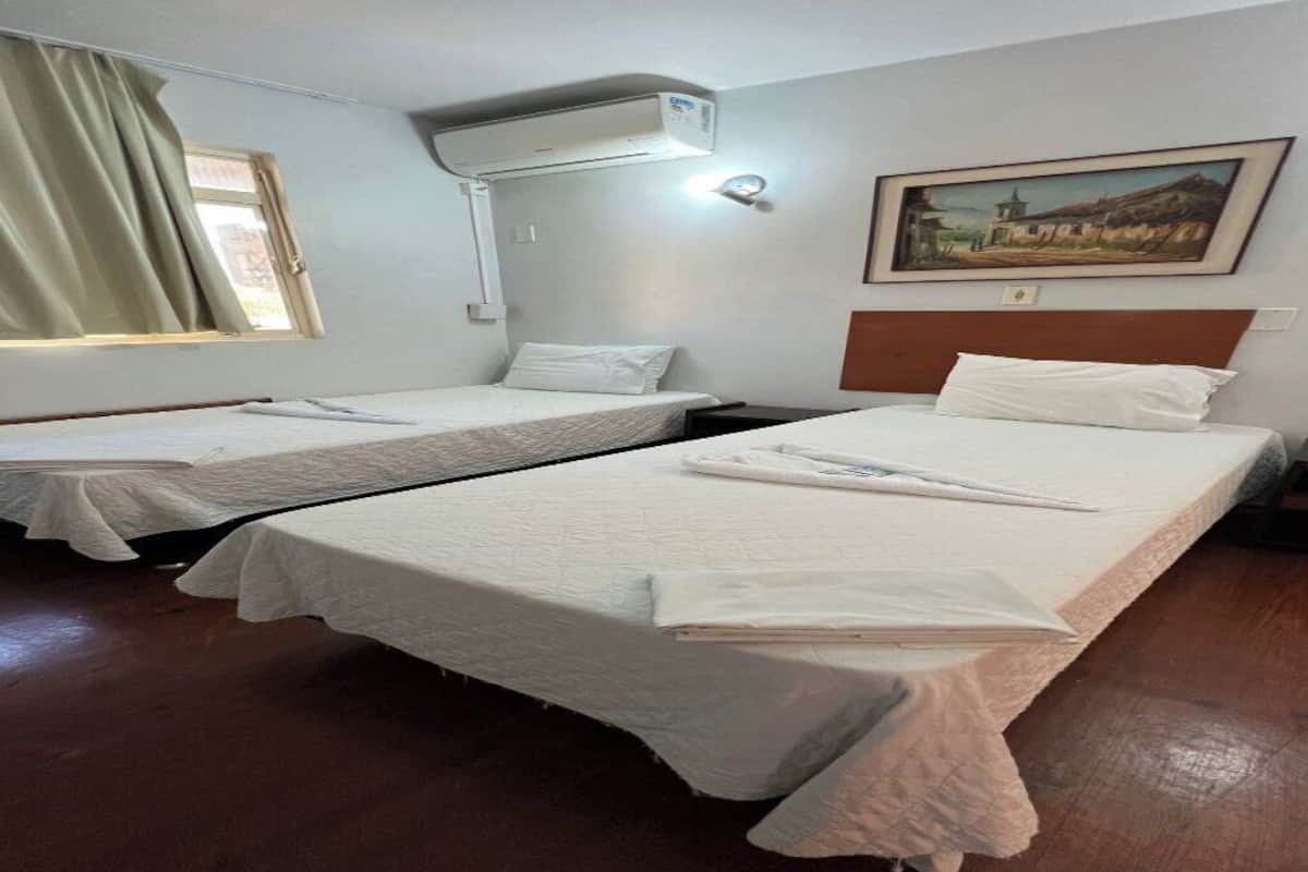 Quarto de hotel com duas camas individuais, janela com cortinas, ar condicionado e um quadro na parede.