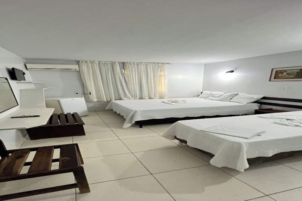 Quarto de hotel com duas camas, uma escrivaninha, uma cadeira e uma televisão.