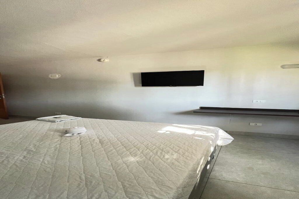 A bedroom with a bed, a flat-screen TV mounted on the wall, and a built-in bench.