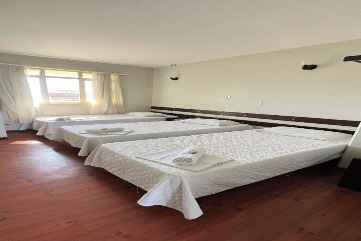 Quarto de hotel com duas camas, uma janela com cortinas e piso de madeira.