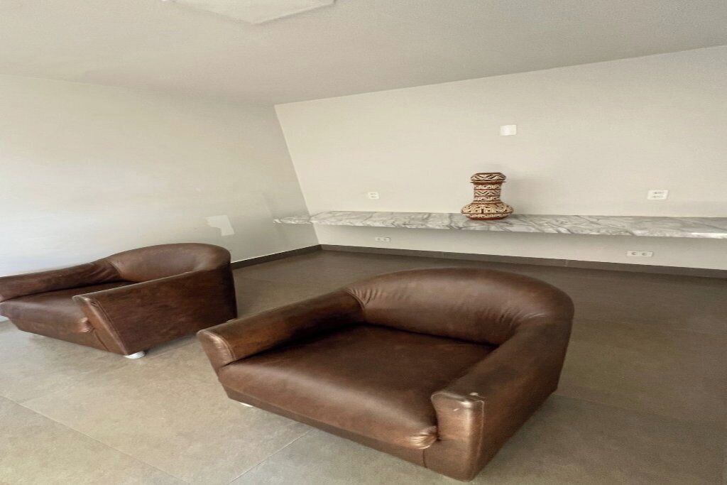 Una sala de estar moderna con dos sofás de cuero marrón, una chimenea de mármol y una pared blanca.