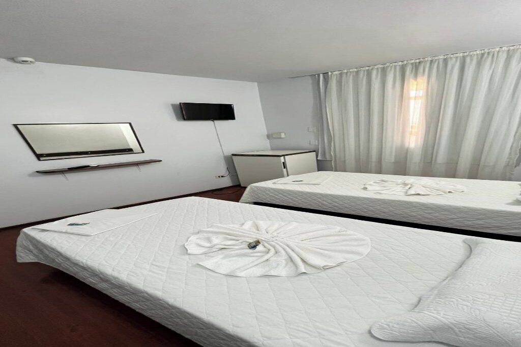 Habitación de hotel con dos camas, un televisor montado en la pared y una ventana con cortinas.