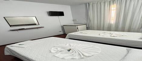 Habitación de hotel con dos camas, un televisor montado en la pared y una ventana con cortinas.