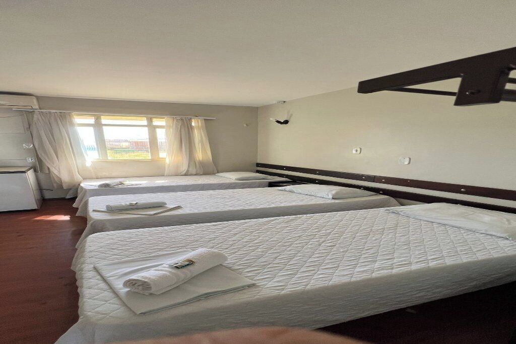 A hotel room with three beds, a desk, and a window with curtains.