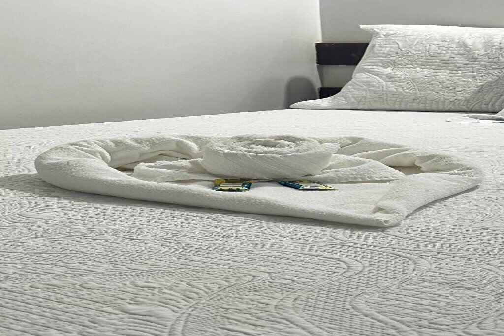 Een net opgemaakt bed met een opgerolde handdoek en een klein decoratief object erop.