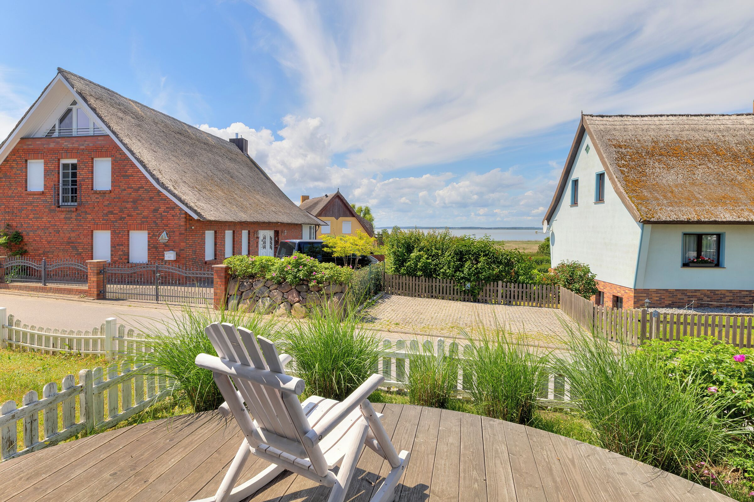 A wooden deck with a rocking chair, a brick house with a thatched roof, and a white house with a similar roof.