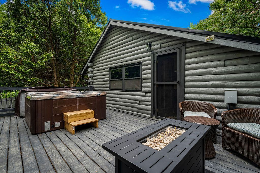 A log cabin with a deck, a hot tub, a fire pit, and wicker furniture.
