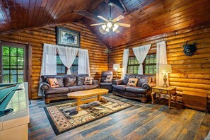 A log cabin interior with a wooden ceiling, leather sofas, a wooden coffee table, and a fireplace. - Cozy Rustic Cabin Close to Town w/Hot Tub & Games (Sevierville)