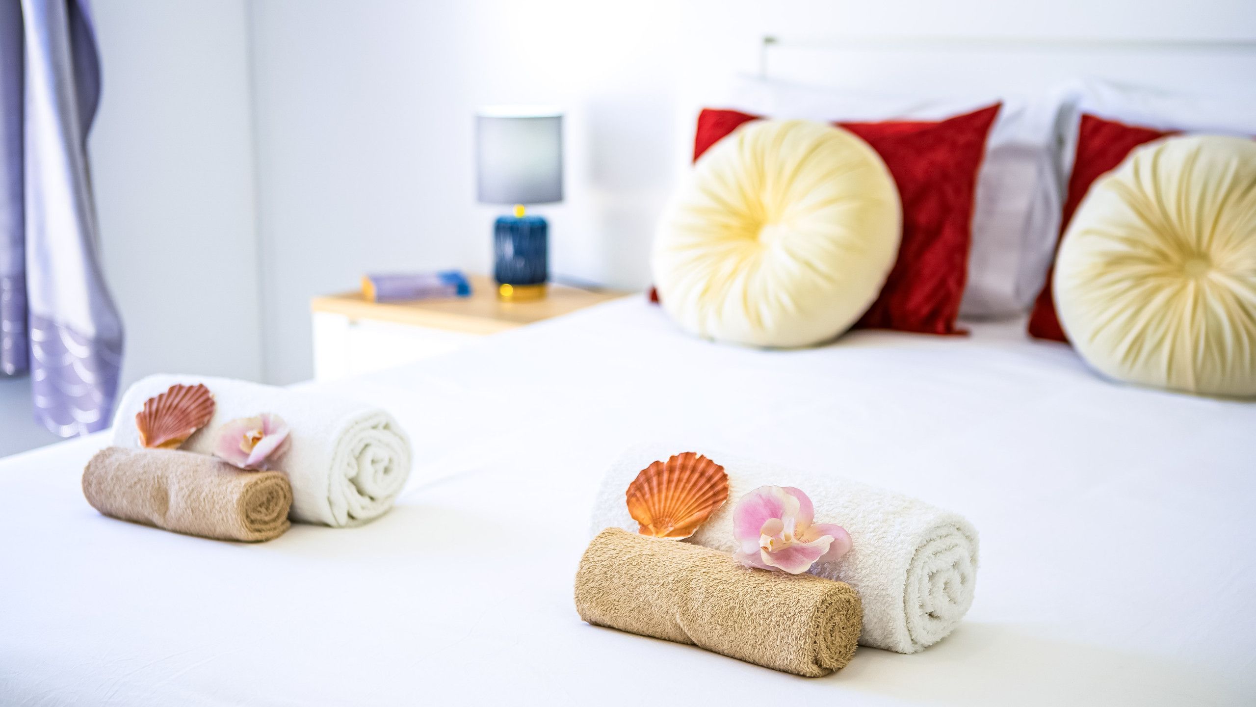 A hotel room with a neatly made bed, pillows, and decorative towels with seashells and flowers.