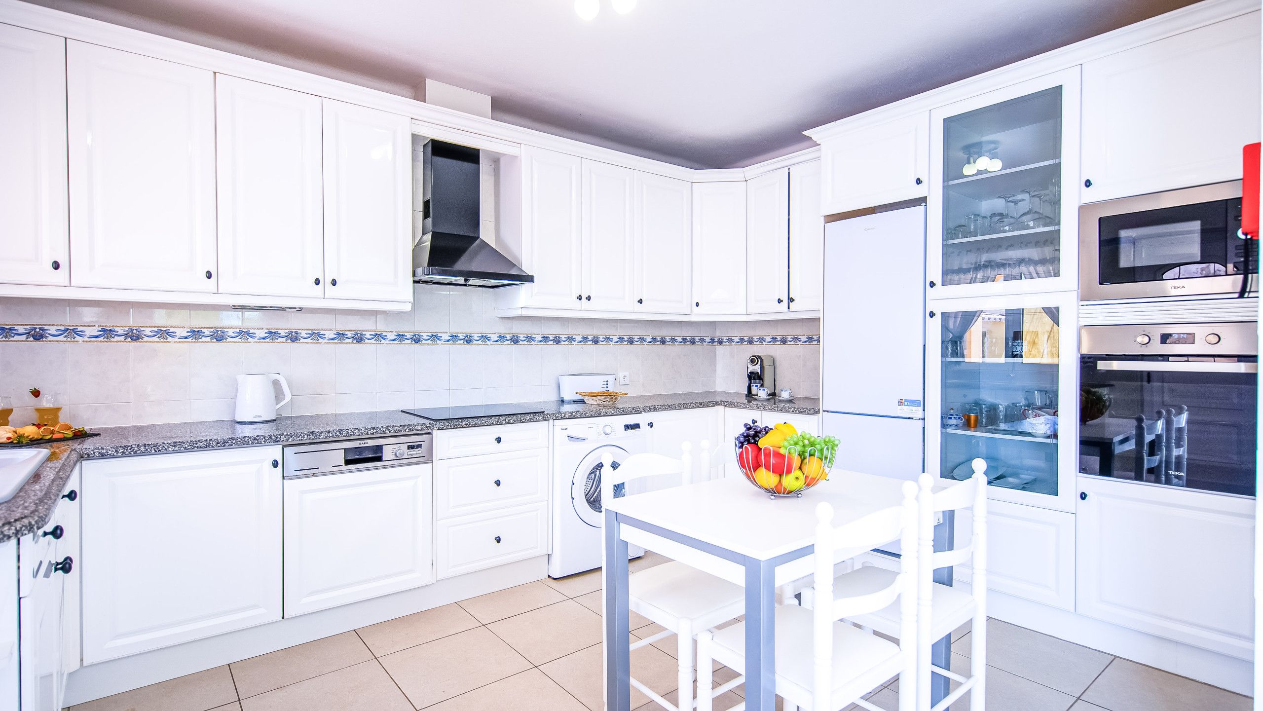 A modern kitchen with white cabinets, a built-in oven, and a dining area with a table and chairs.