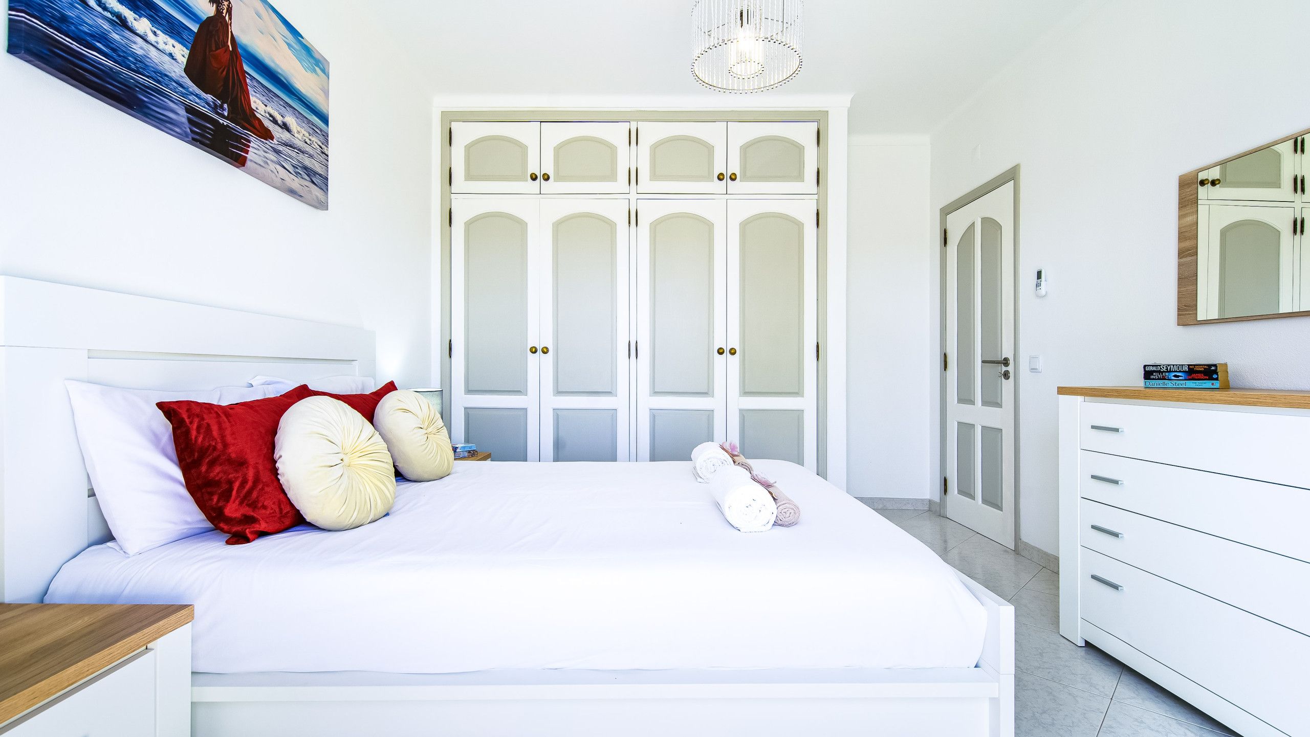 A bedroom with a bed, a nightstand, a dresser, a mirror, and a painting on the wall.