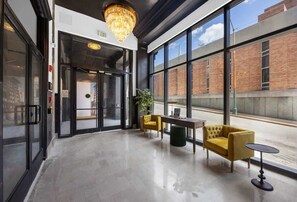 A modern lobby with a chandelier, a glass door entrance, and a seating area with yellow chairs and a table. - Downtown Modern Studio at Historic Park Hotel (Chattanooga)