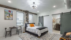 Ein modernes Schlafzimmer mit Bett, Schreibtisch und Stuhl, einem großen Fenster und einer Kristallleuchtre.'