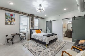 A modern bedroom with a bed, a desk, and a chair, a large window, and a chandelier. - Park Hotel Studio Suite 607 (Chattanooga)